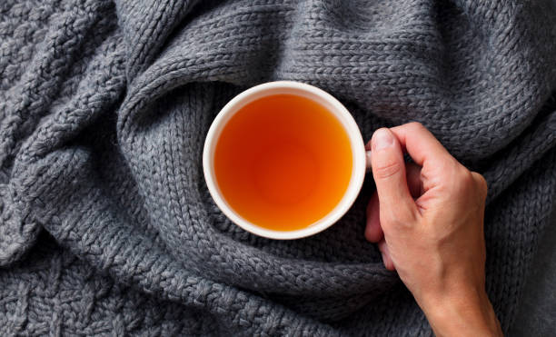 istock Tea cup in female hand on knitted scarf. Grey background. Top view. 1188641746
