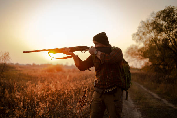 young irish looking man with a reed, backpack and ammunition belt,  hunting at the countryside near the track in the picturesque sunset rays - bird hunter imagens e fotografias de stock