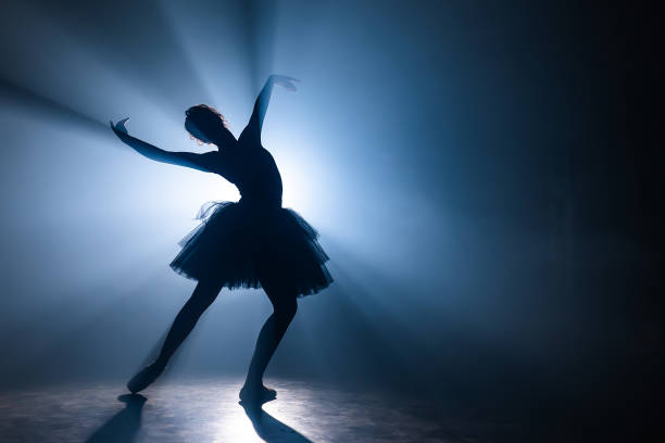 ballerine dans la robe noire de tutu dansant sur l'étape avec la lumière bleue magique et la fumée. silhouette de jeune danseur attirant dans des chaussures de ballet pointe exécutant dans l'obscurité. copiez l'espace. - round toe shoes photos et images de collection