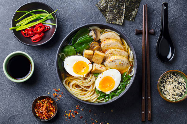soupe asiatique de nouilles, ramen avec du poulet, du tofu, des légumes et des œufs dans un bol noir. fond d'ardoise. vue du haut. - soup chicken soup chicken noodle soup food photos et images de collection