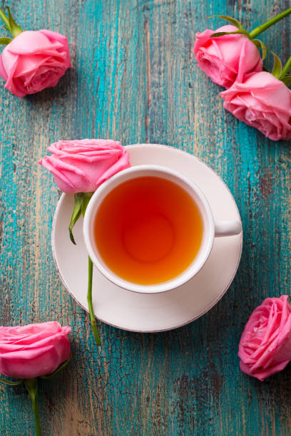 Cup of tea with pink rose. Colorful turquoise wooden background. Top view. Cup of tea with pink rose. Colorful turquoise wooden background. Top view pink tea stock pictures, royalty-free photos & images