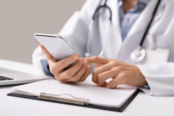 Photo of Male doctor using smartphone at workplace, making online consultation