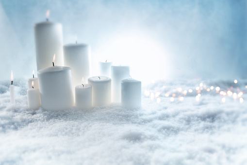 Festive white candles decorated in snow with bright bokeh at christmas time