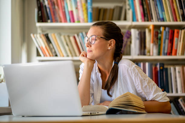 deconcentrated Young Adult Woman Looking Away While Studying in Library deconcentrated Young Adult Woman Looking Away While Studying in Library. casarsaguru stock pictures, royalty-free photos & images