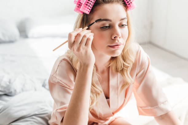 beautiful woman in pink hair curlers styling eyebrows in bedroom beautiful woman in pink hair curlers styling eyebrows in bedroom curling tongs photos stock pictures, royalty-free photos & images