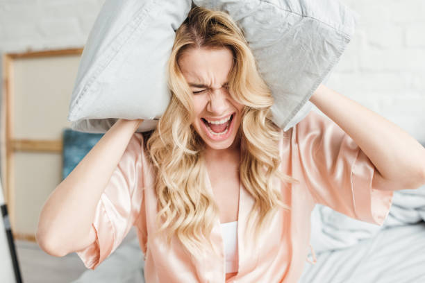 emotional woman in silk robe holding pillow screaming in bedroom - one woman only young women people nightie imagens e fotografias de stock