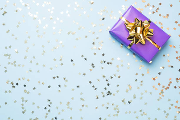 płaskie tło świeckie dla obchodów bożego narodzenia i nowego roku. pudełka na prezenty są fioletowe ze złotymi wstążkami i gwiazdkami konfetti na niebieskim tle. spacja na kopiowanie z góry. - gift purple turquoise box zdjęcia i obrazy z banku zdjęć