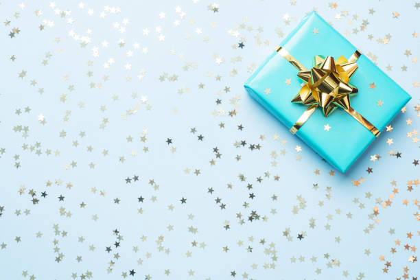 квартира лежал фон для празднования рождества и нового года. подарочная коробка бирюзовая с золотыми лентами луки и конфетти звезды на син� - gift purple turquoise box стоковые фото и изображения