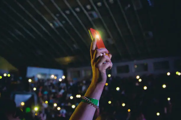 Smartphone with a turned on flashlight in a female hand at a concert.
