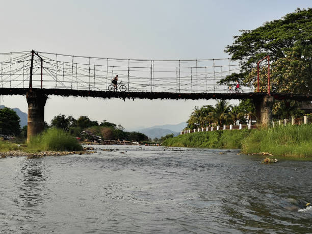 Man cycling on footbridge across the Nam Song River, a small river that flows through the town of Vang Vieng, a popular tourist destination in Laos.