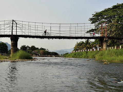 Man cycling on footbridge across the Nam Song River, a small river that flows through the town of Vang Vieng, a popular tourist destination in Laos.
