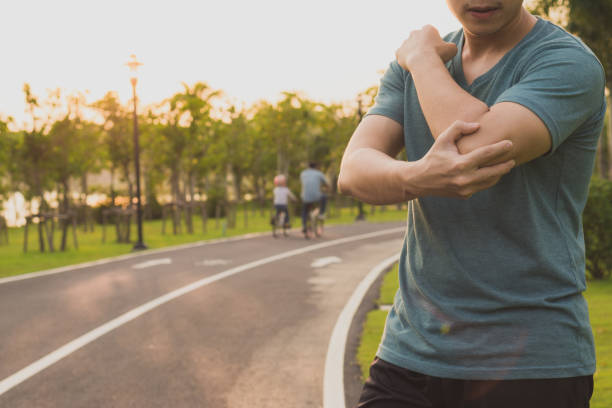 ein männlicher athlet, der unter arm- und ellbogenschmerzen und verletzungen im park leidet. sport- und gesundheitskonzept. - ellenbogen stock-fotos und bilder