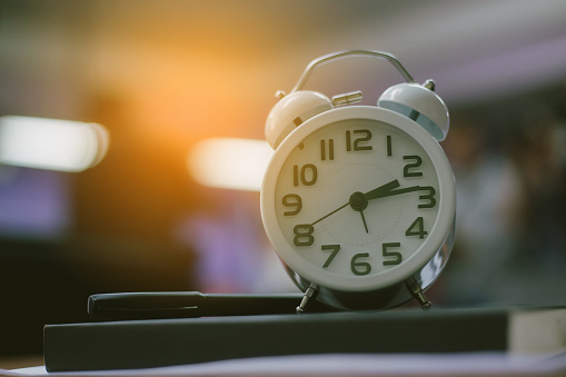 retro clock time at 9 o'clock with notebook or memo on wood table, times of memory writing diary concept vintage color tone.