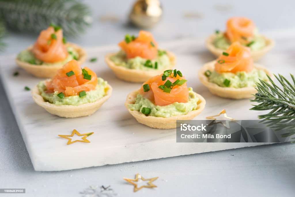 Canapes with smoked salmon, cream cheese and avocado on light background with space for text. Christmas and new year holidays background concept. Starters snacks recipe ideas. Canapes with smoked salmon, cream cheese and avocado on light background with copy space. Christmas and new year holidays background concept. Starters snacks recipe ideas. Christmas Stock Photo