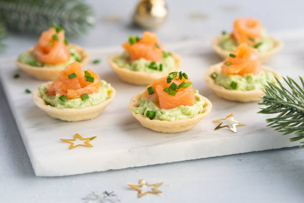 Canapes with smoked salmon, cream cheese and avocado on light background with space for text. Christmas and new year holidays background concept. Starters snacks recipe ideas. Canapes with smoked salmon, cream cheese and avocado on light background with copy space. Christmas and new year holidays background concept. Starters snacks recipe ideas. restaurant food canapes appetizers stock pictures, royalty-free photos & images