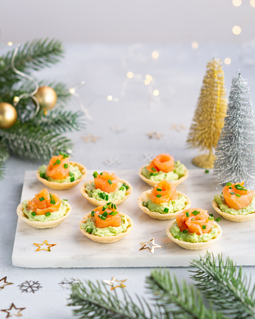 Canapes with smoked salmon, cream cheese and avocado on light background with copy space. Christmas and new year holidays background concept. Starters snacks recipe ideas.