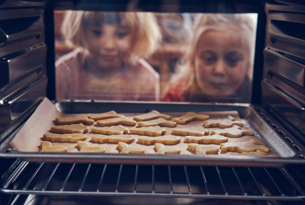 오븐에서 크리스마스 쿠키를 굽는 어린 소녀 - pastry cutter family holiday child 뉴스 사진 이미지