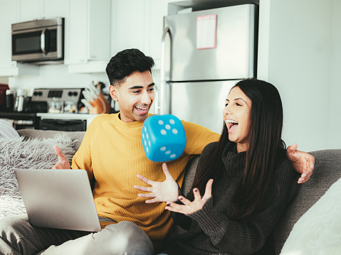 Young Indian couple working on laptop inside their apartment. View of the modern penthouse apartment in the background.