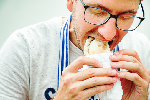 Close-up on young man biting into an empanada tucumana wrapped in paper.