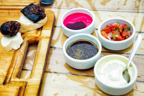 Argentinian morcilla, a Latin kind of blood sausage. on bread with four condiments in small ceramic pots: chimichurri, a lemon mayonnaise, a beet mayonnaise and a tomato and onions salsa.