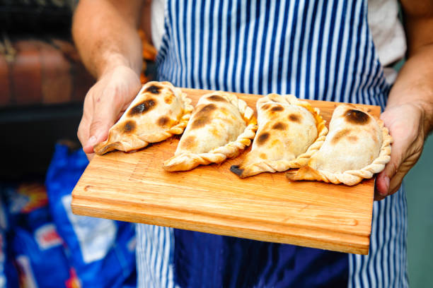 Close-up on perfectly baked empanadas tucumanas on a cutting board held by baker Close-up on perfectly baked empanadas tucumanas on a cutting board held by baker outdoors. argentinian culture stock pictures, royalty-free photos & images