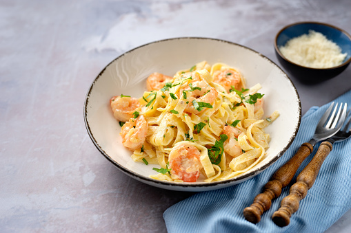 Tasty shrimp fettuccine alfredo with parmesan on light blue background
