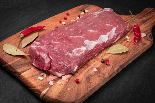 Raw lamb tenderloin fillet or mutton sirloin meat on black stone plate background. Fresh sheep fillet, loin filet with spices on a wooden cutting board closeup