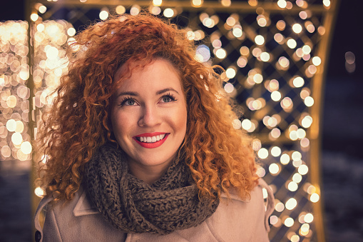 Christmas portrait of young beautiful woman with red curly hair outdoors at night