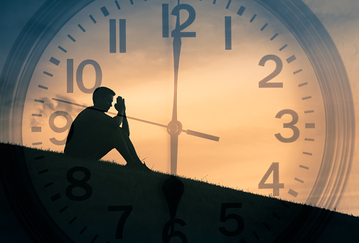 Double exposure of young man praying outdoors with clock in the background.