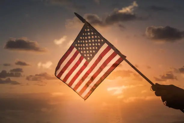 Photo of Person holding USA American flag on sunset background.