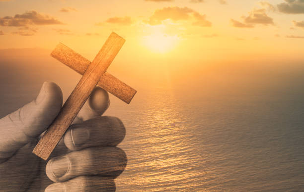 Hand holding wooden cross on sunset background. Double exposure image.