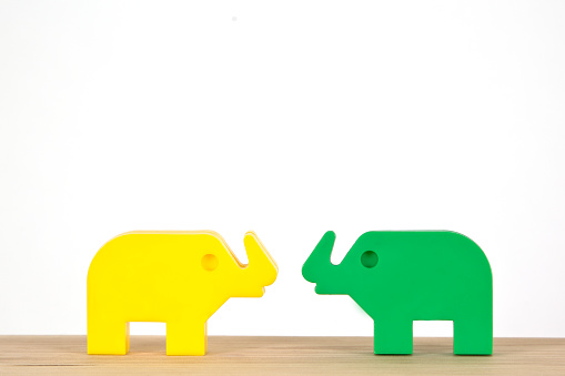 pair of vintage plastic toy elephants in yellow and green on white background looking at each other