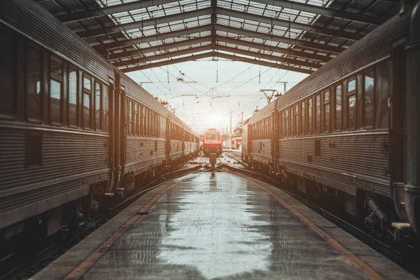 Symmetrical view of a railroad station depot with a triangle roof above, a modern red locomotive being in a defocused background on maintenance, two high-speed trains on both sides of the platform
