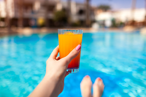 Woman holds a layered cocktail on swimming pool background. All inclusive concept