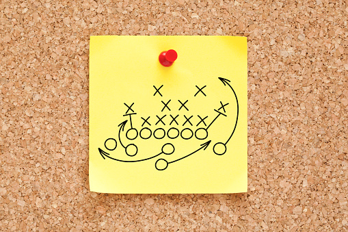 American football or rugby game playbook, strategy or tactics drawn on yellow sticky note pinned on bulletin cork board.