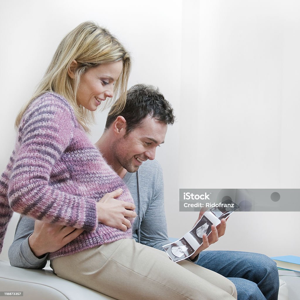 Smiling pregnant couple with ultrasound scan Young smiling couple holding an ultrasound scan of their expecting baby at home. 20-29 Years Stock Photo