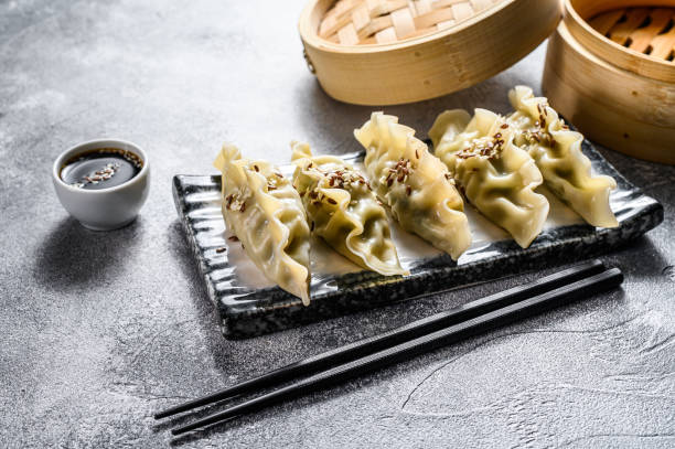 istock Korean dumplings on a ceramic plate. Black chopsticks and a bamboo steamer. Gray background. Top view. 1188737491