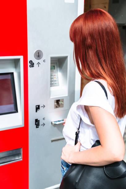 istock Young redhead woman inserts banknote into terminal 1188739239