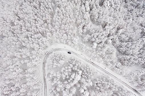 Car on road in winter trough a forest covered with snow. Aerial photography of a road in wintertime trough a forest covered in snow. High mountain pass.