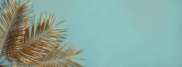 istock Three gold painted date palm leaves on desaturated turquoise background 1188744226