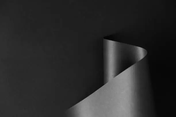 Glossy black monochrome paper wave on dark background. Geometrical minimalist style backdrop.