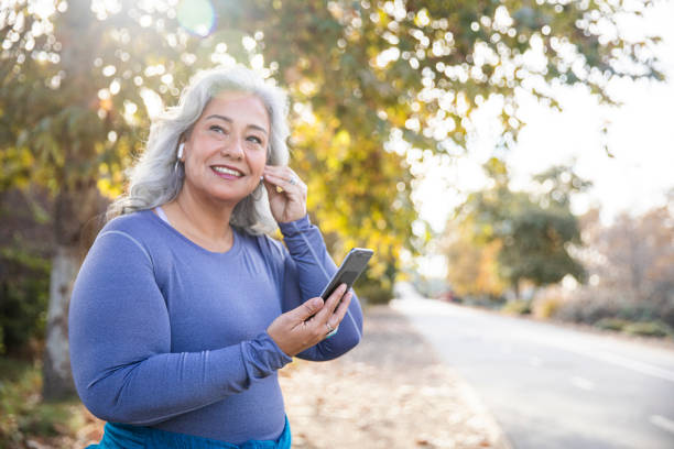 ワークアウトの準備をしているスマートフォンを持つ美しい女性 - mature adult audio ストックフォトと画像