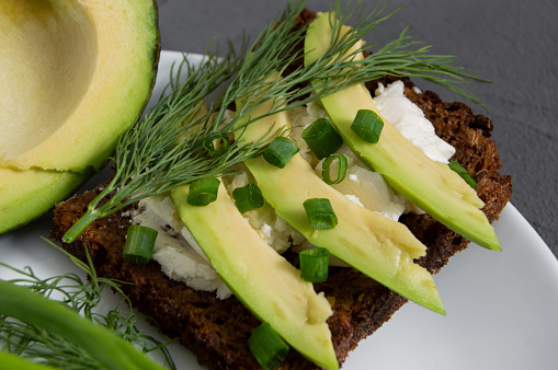 Vegetarian sandwich with cream cheese and avocado slices with dill and green onion close up on plate