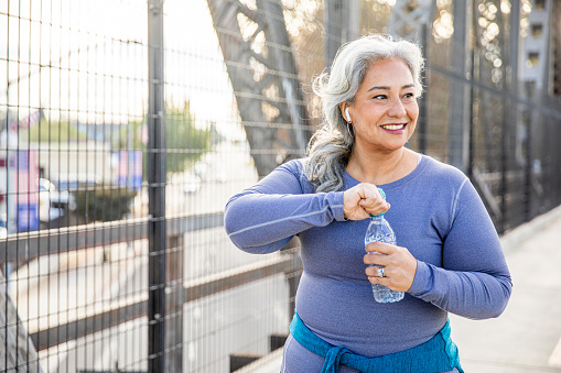 A senior Mexican woman drinking water after a workout