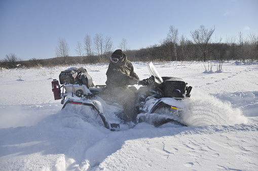 ATV on tracks ride back in a deep snow in the taiga. White field is around. Winter travel in the Khabarovsk Territory