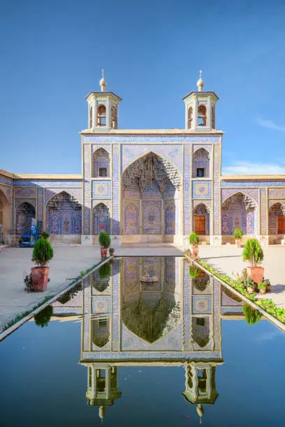 Awesome view of the Nasir al-Mulk Mosque (Pink Mosque) reflected in pool in the middle of traditional courtyard in Shiraz, Iran. Amazing Persian exterior of the Muslim place. Islamic architecture.