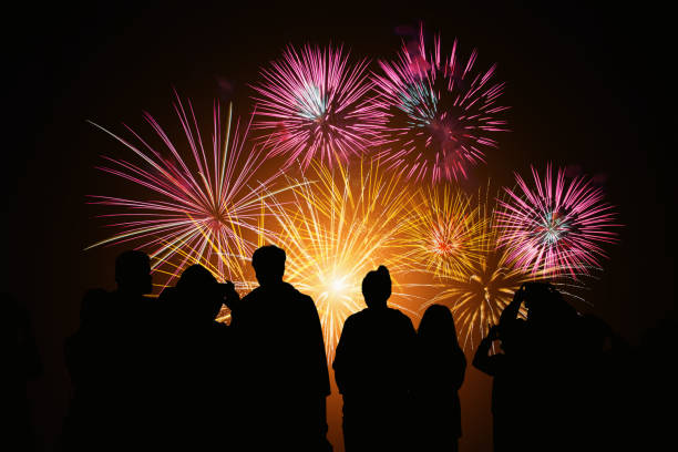 Crowd watching fireworks and celebration. Happy family sitting on floor and watching the fireworks Celebration at night on New Year and copy space - abstract holiday background. Crowd watching fireworks and celebration. Happy family sitting on floor and watching the fireworks Celebration at night on New Year and copy space - abstract holiday background. new year urban scene horizontal people stock pictures, royalty-free photos & images