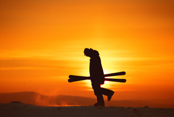 Skiers silhouette goes with ski in hands against sunset sky and sun