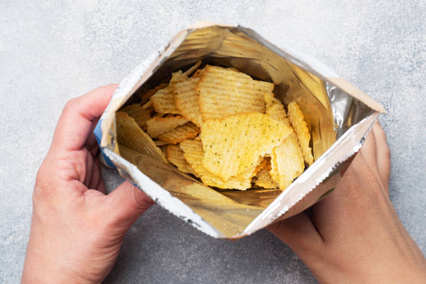 картофельные чипсы с пряным в открытой упаковке держатся за руки. закройте выборочный фокус. - potato chip стоковые фото и изображения