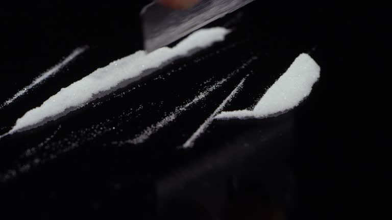 A small mound of cocaine getting cut into lines on a mirrored surface